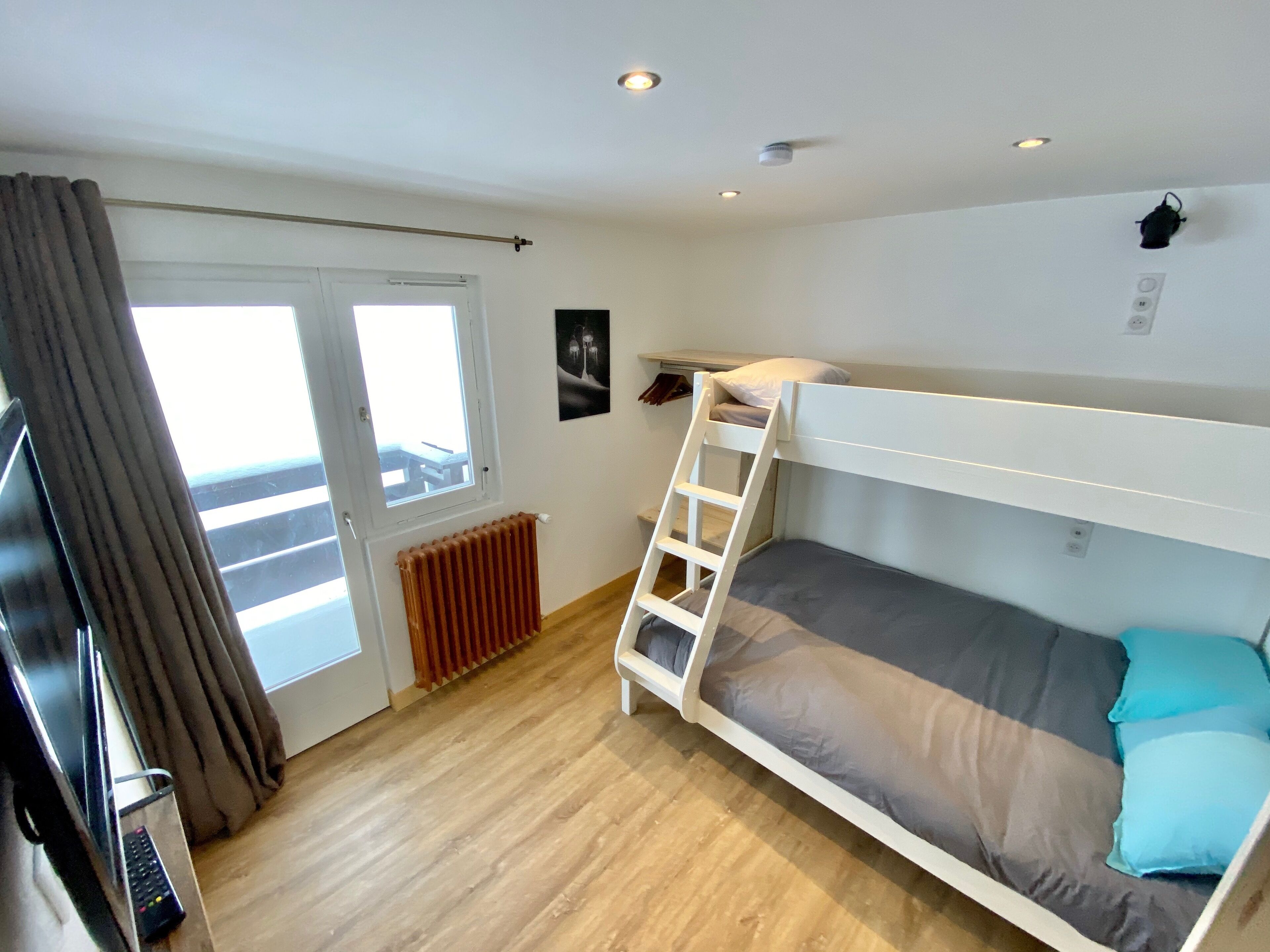 Une chambre avec un lit superposé, une fenêtre, un radiateur et un téléviseur.