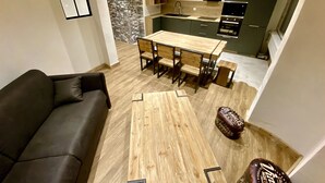 Un soggiorno moderno con un divano, un tavolo da pranzo in legno e sedie, e una cucina sullo sfondo.