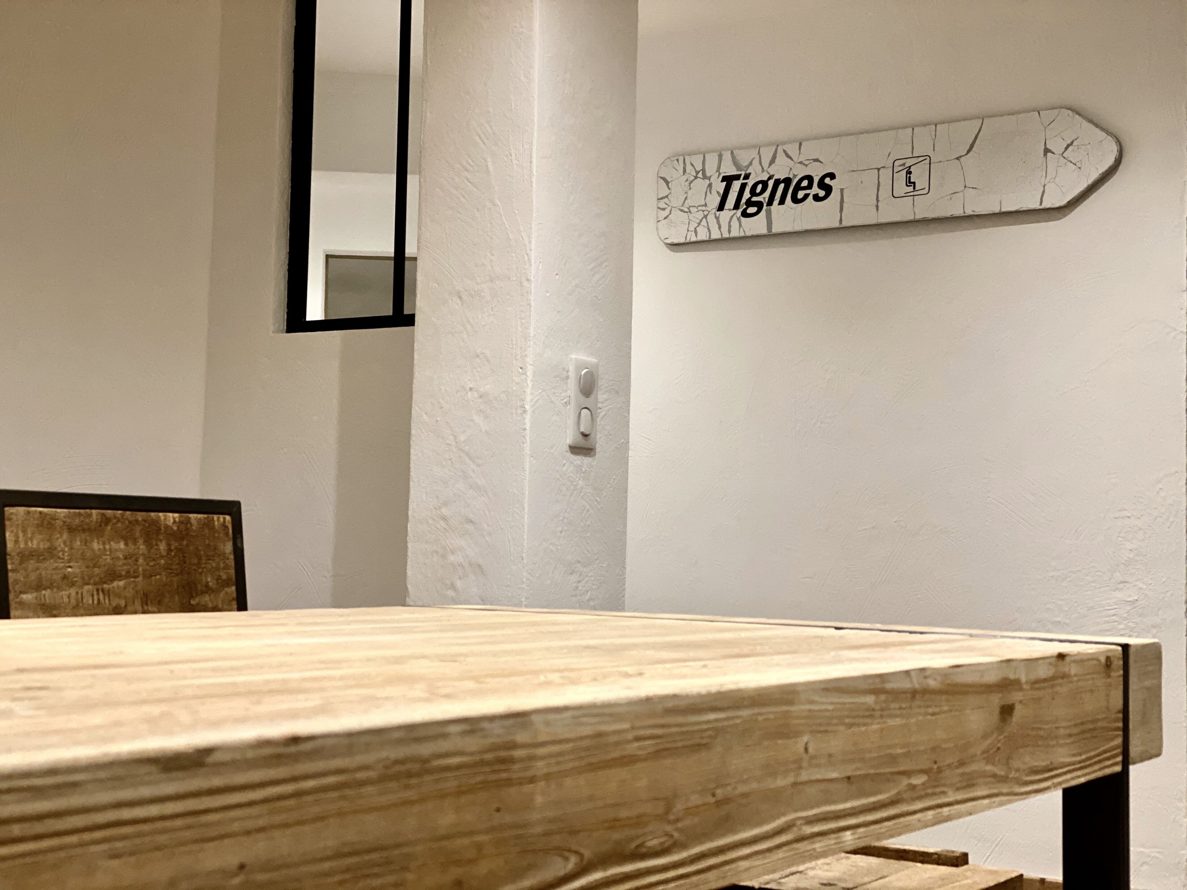 A wooden table with a white wall in the background, a whiteboard with the word 'Tignes' and a ski icon, and a light switch.