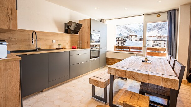 Una cucina moderna con isola in legno, mobili grigi e un'ampia finestra vista montagna.