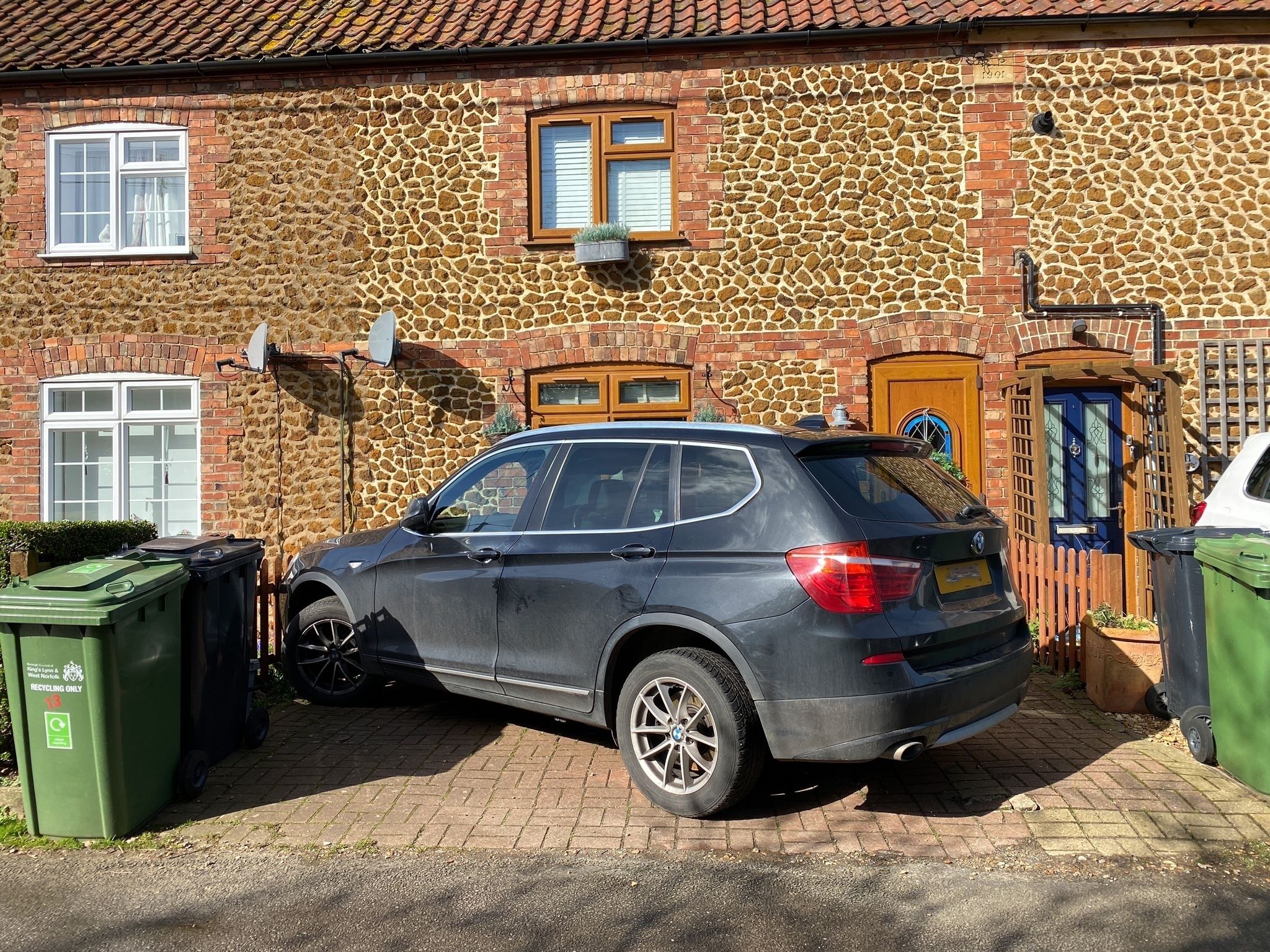 A black SUV parked in front of a stone building with a tiled roof, a wooden door, and a satellite dish.