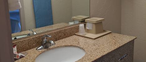 A bathroom with a granite countertop sink, a mirror, a towel rack, and a wooden hanger rack.