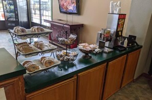 A breakfast buffet with pastries, a coffee machine, and a TV screen.