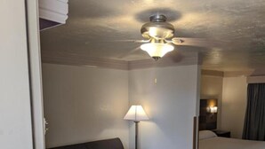 A compact hotel room with a sofa, a small table, a bed, and a ceiling fan. - Atrium Inn (Fort Stockton)