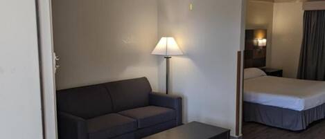 A compact hotel room with a sofa, a small table, a bed, and a ceiling fan.