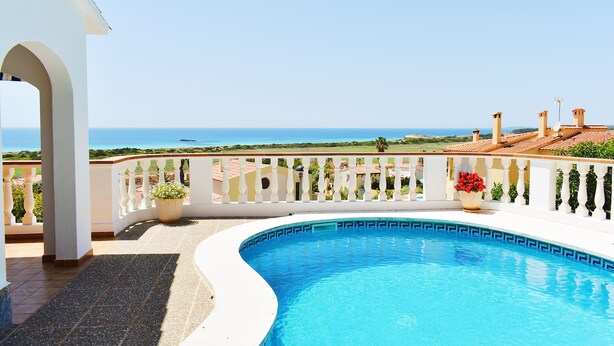A swimming pool with a curved edge, a white balcony with a railing, and a view of the sea. - Villa Maria, incredible sea views, relax, swimming pool, wifi, barbecue, garden (alaior)