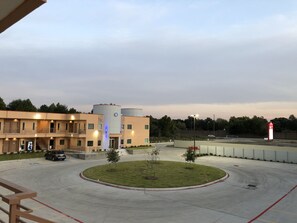 A multi-story hotel with a parking area, a landscaped circular garden, and a large building with cylindrical structures. - Crystal Inn (Houston)