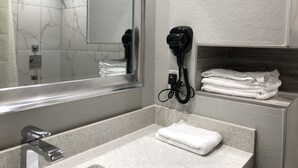 Ein Badezimmer mit großem Spiegel, Waschbecken, Handtuchhalter und Haartrockner.