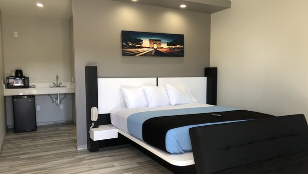 Ein modernes Hotelzimmer mit Bett, Nachttisch und einer kleinen Küchenzeile.