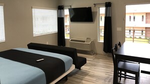 Ein Hotelzimmer mit zwei Betten, einem Fernseher, einem Tisch und Blick nach draußen.