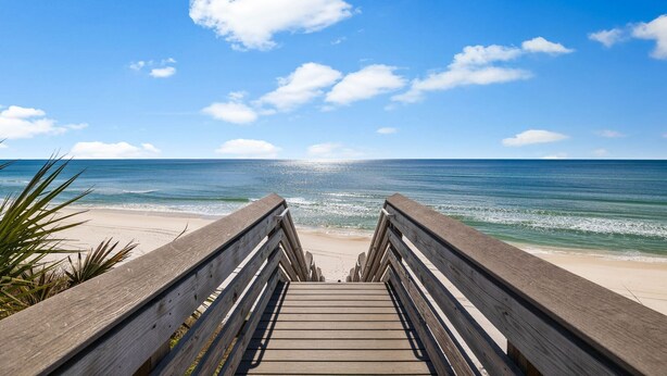 Un muelle de madera que conduce a una playa con cielo azul despejado y océano.