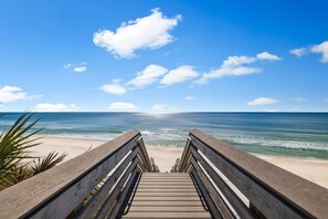 A wooden boardwalk leading to a beach with a clear blue sky and ocean.