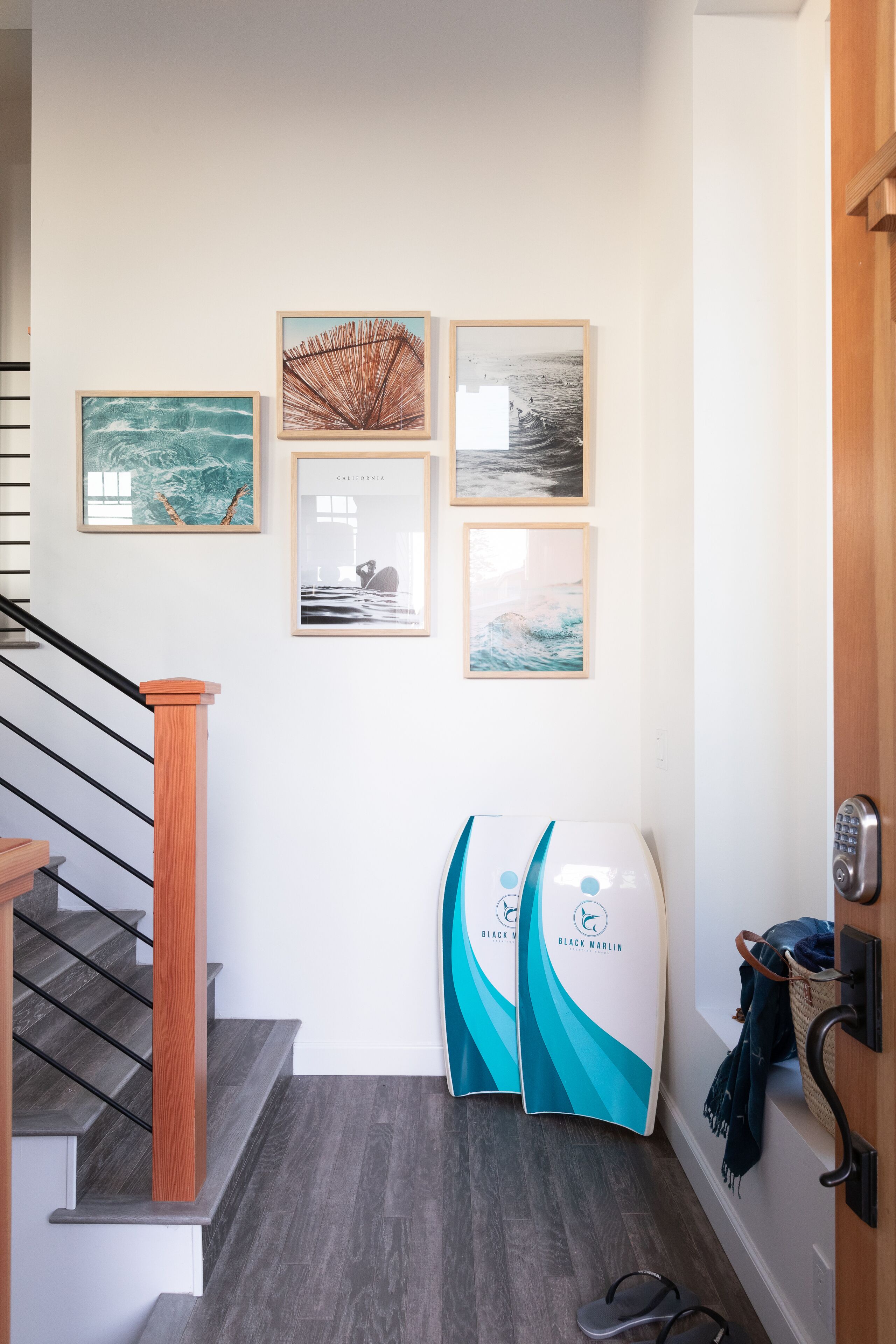 Un couloir avec un escalier, un mur orné de tableaux encadrés et une porte avec un porte-serviettes.