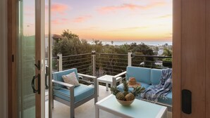 Ein Balkon mit blauen Sitzgelegenheiten, einem Tisch mit einer Ananas als Mittelpunkt und Blick auf den Sonnenuntergang über dem Meer.