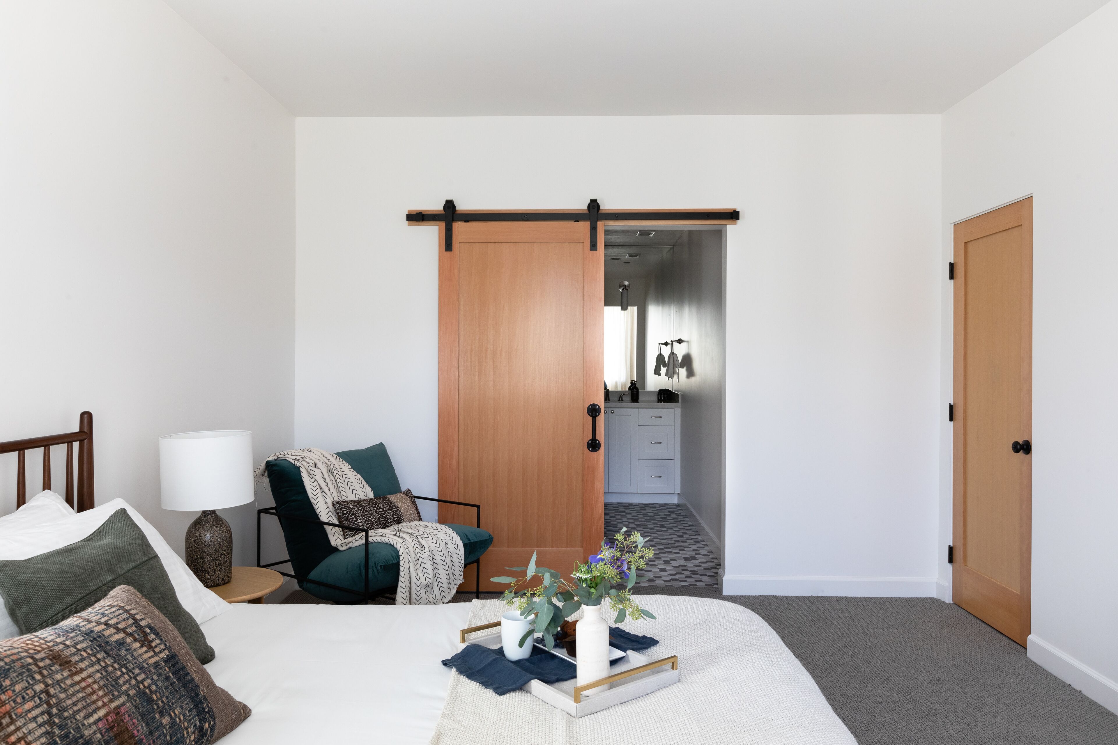 Une chambre à coucher comprenant un lit, une table de chevet, une lampe, une chaise et une porte coulissante donnant sur une salle de bain.