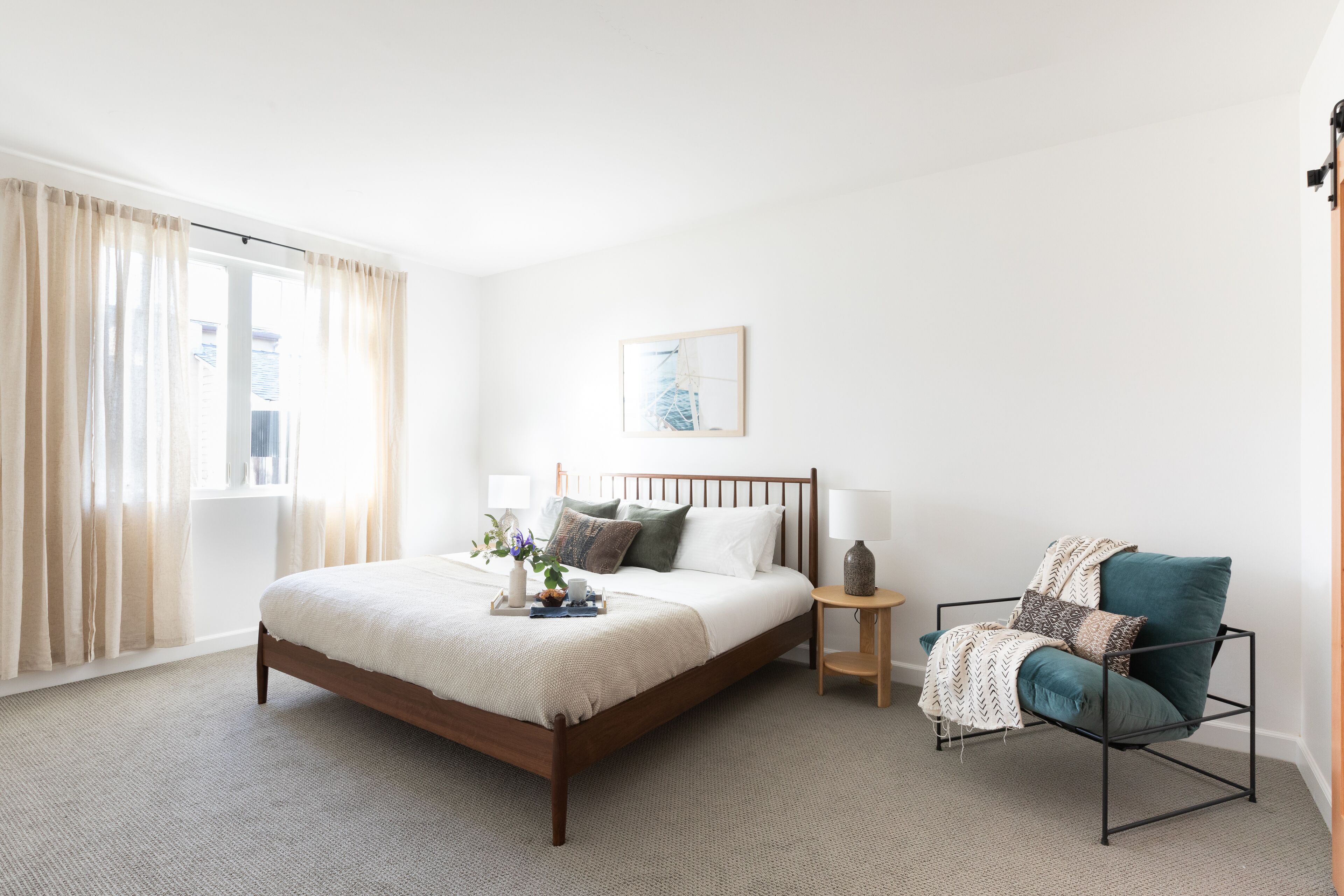 A bedroom with a wooden bed, a bedside table, a chair, and a window with curtains.