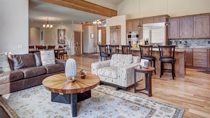 A spacious living room with a large wooden coffee table, a patterned sofa, and a dining area with chairs and a table. - Riverwood Retreat-4BR Warrior's Mark Home, Private Hot Tub, Fireplace, Sleeps 12 (Breckenridge)