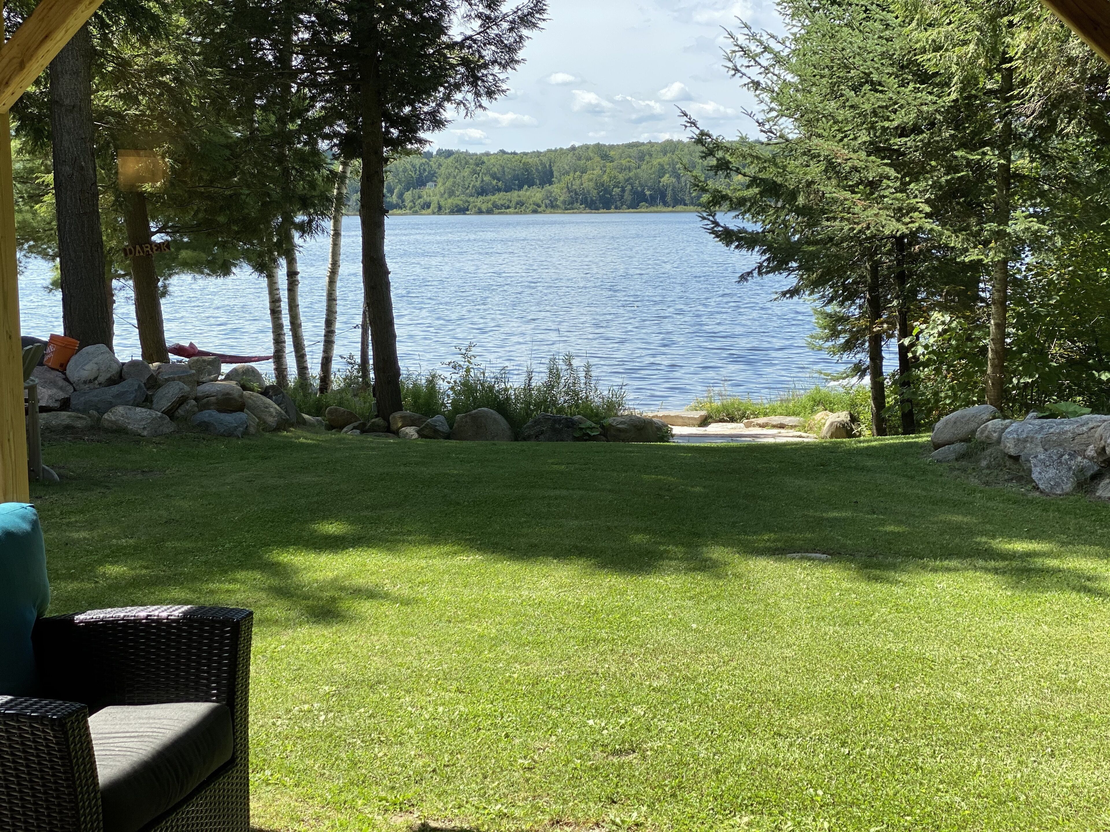 Ett grönområde med utsikt över en sjö, omgivet av träd och en träkonstruktion.