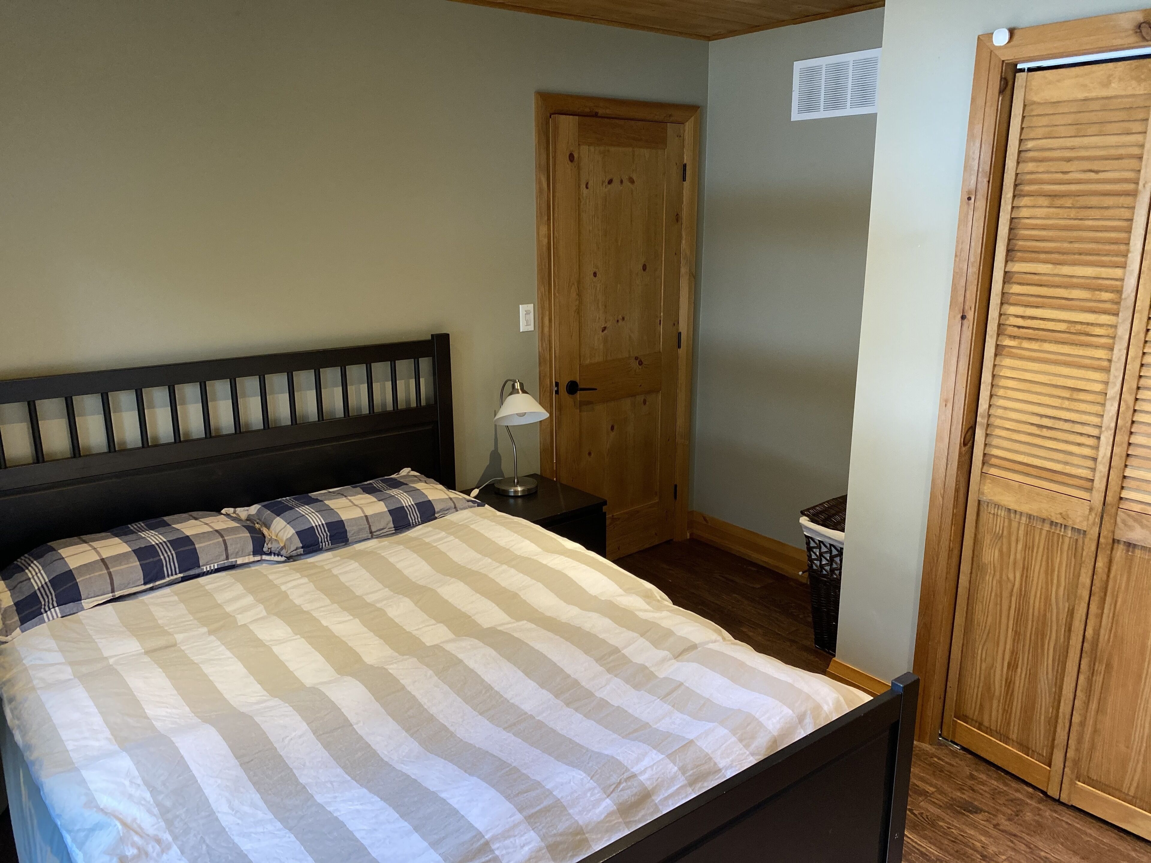 A bedroom with a bed, a nightstand, a lamp, a wooden door, and a wardrobe.