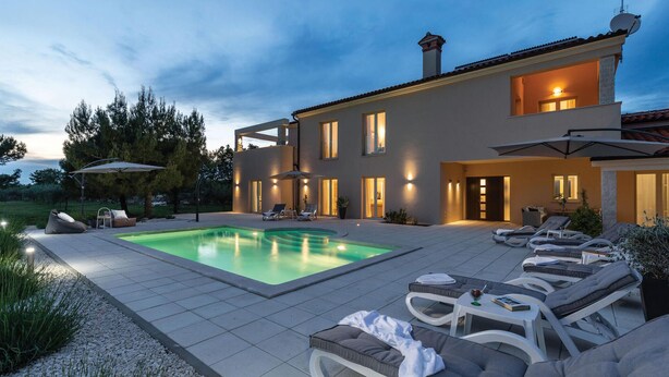 Una casa moderna con piscina, zona de estar exterior y un patio bien iluminado.