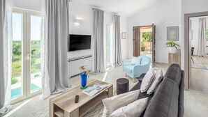 Una sala de estar moderna con un televisor de pantalla plana, un sillón azul, un sofá gris y una mesa de centro de madera.