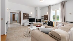 Una sala de estar moderna con sofá, televisor, chimenea y ventanas amplias.