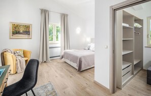 Un dormitorio con cama, escritorio, silla, armario y ventana con cortinas.