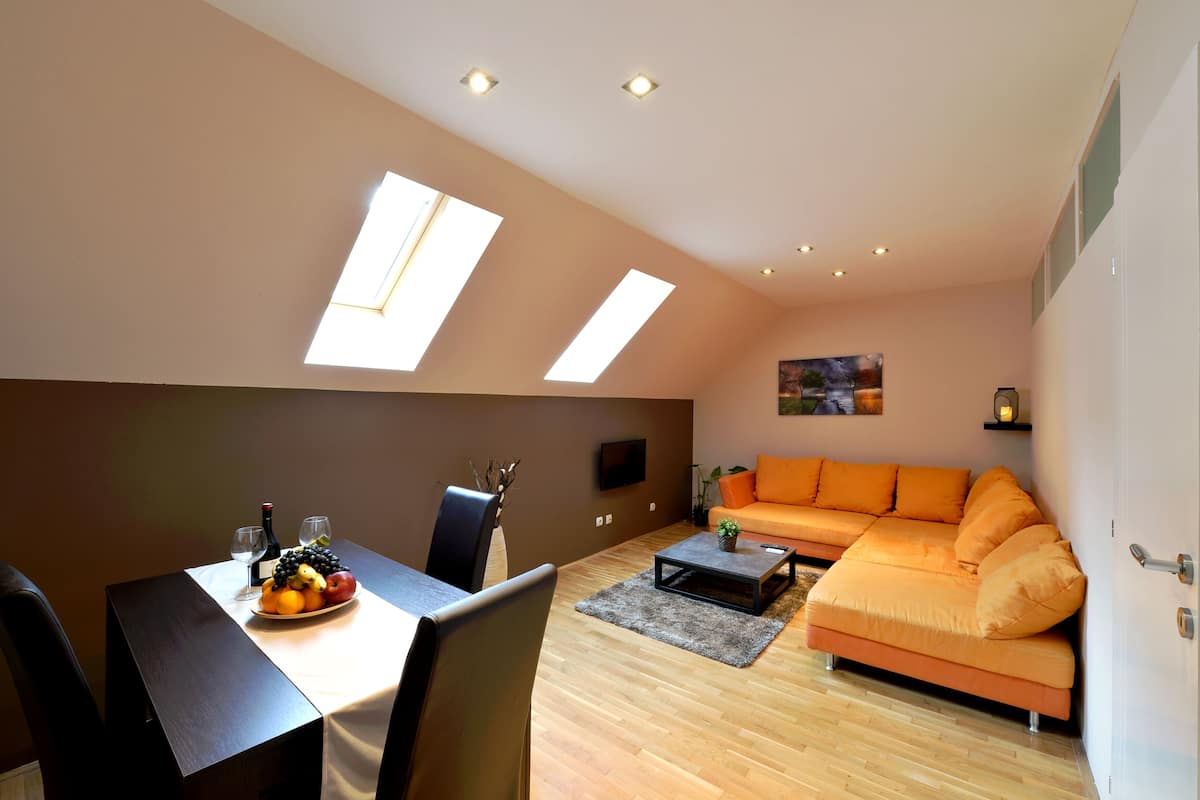A modern living room with a dining table, orange sofa, and skylights.