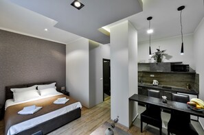 A modern hotel room with a bed, bedside table, and a kitchenette area. - Apartments Savamala center (Belgrade)