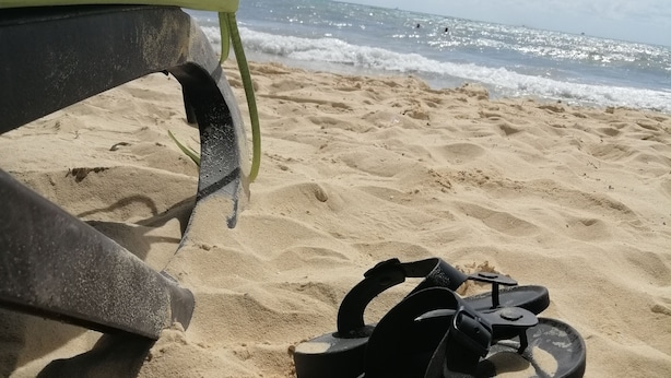 A pair of black sandals on a sandy beach with a surfboard and a shovel nearby. - Nikis place a nice place to be relax at the riviera maya (Playacar)