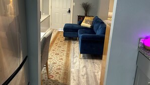Eine kleine Küche mit einem Kühlschrank, ein Essbereich mit Teppich und ein blaues Sofa im Wohnzimmer.
