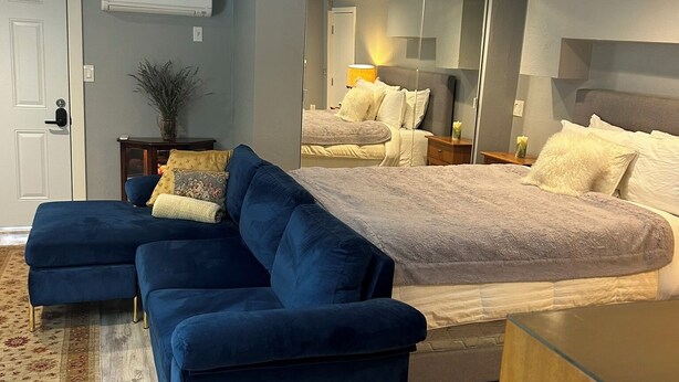 Ein modernes Schlafzimmer mit einem großen Bett, einem blauen Sofa und einem Spiegel, der den Raum widergibt.