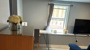 Ein modernes Wohnzimmer mit Schreibtisch aus Holz, einem blauen Sofa, einem Fernseher und einem Fenster mit Vorhängen.