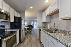 A modern kitchen with white cabinets, a granite countertop, stainless steel appliances, and a dining area in the background. - Glam R Us - Pool - Fabulous Location! Must Stay! (Branson)