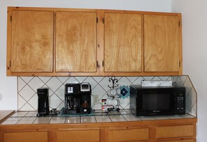 Kitchen area with a countertop, coffee makers, microwave, and mugs.
