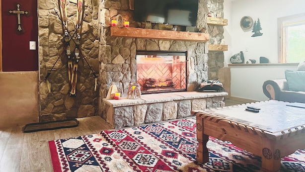 Una chimenea de piedra con un televisor encima, esquíes apoyados en la pared y una alfombra estampada en el suelo.