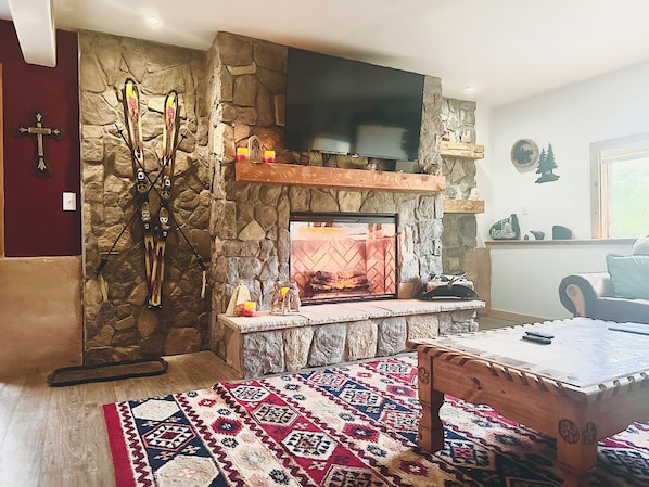 A stone fireplace with a TV above it, skis leaning against the wall, and a patterned rug on the floor.