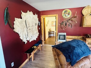 Een kamer met een rode muur, een bankje, een bed met een blauwe deken, een wanddecoratie en een dromenvanger.