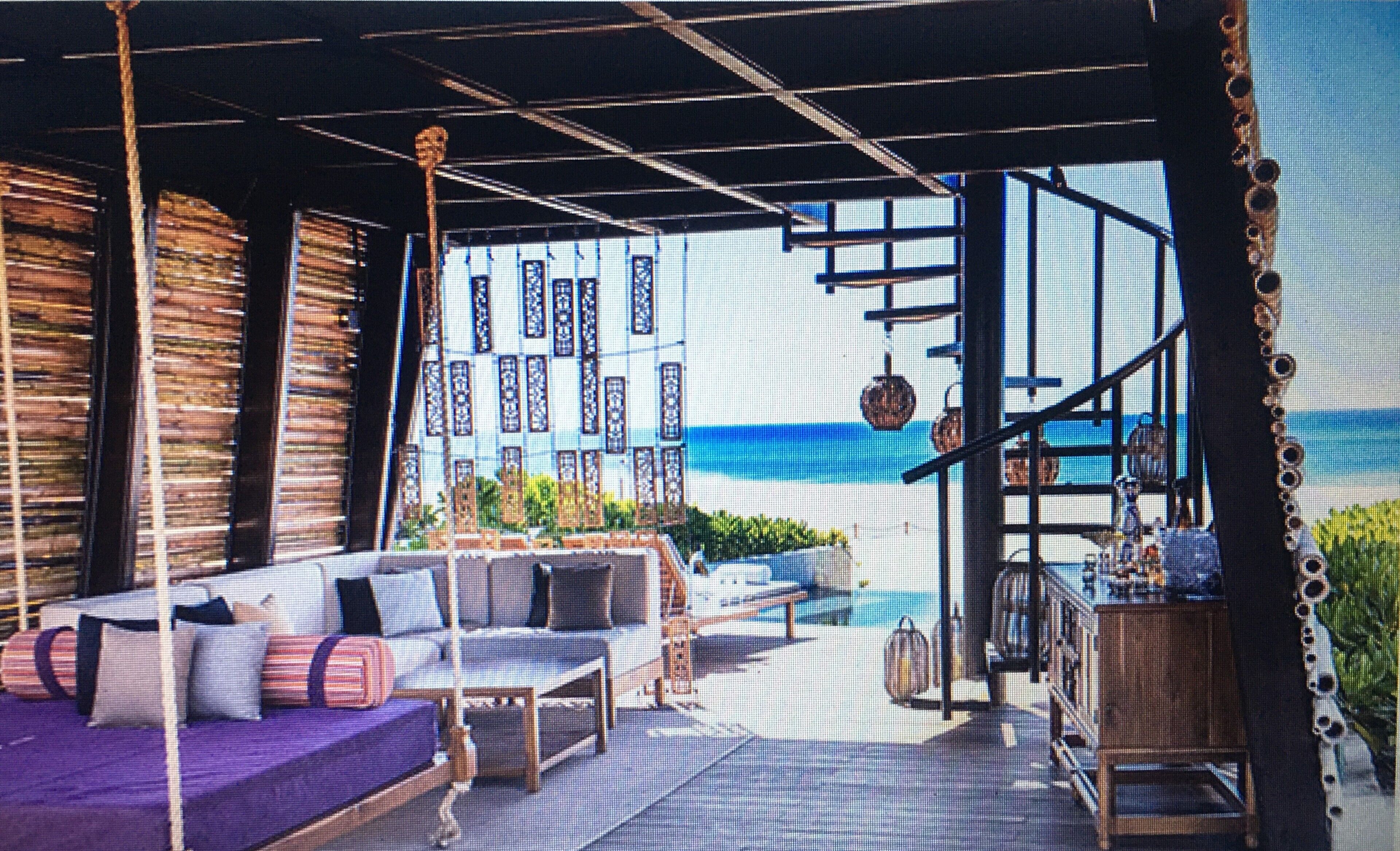 A beachside lounge with a view of the ocean, featuring a sofa set, a wooden table, and a hanging chair.