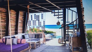 A beachside lounge with a view of the ocean, featuring a sofa set, a wooden table, and a hanging chair.