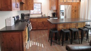 A kitchen with wooden cabinets, a stove, a microwave, a refrigerator, and bar stools. - 2+2, Spa, Sleeps 6, Walk 2 Hiking & Biking Trails, Pet Friendly on North Shore (Big Bear)
