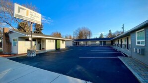 A motel with a signboard, a parking lot, and a building with multiple rooms. - North Idaho Inn (Coeur d'Alene)