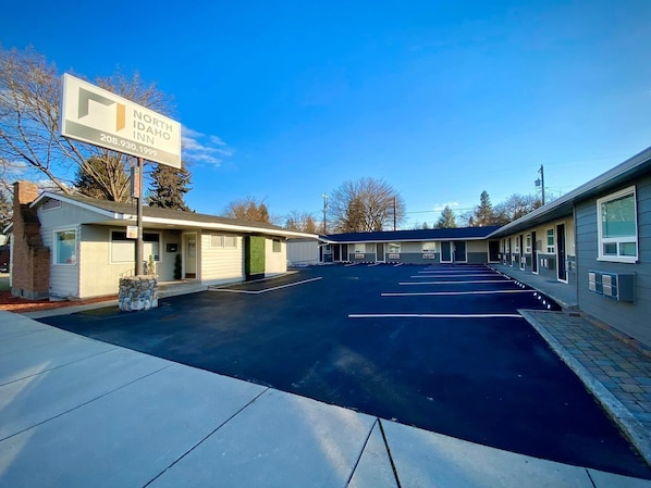 A motel with a signboard, a parking lot, and a building with multiple rooms.