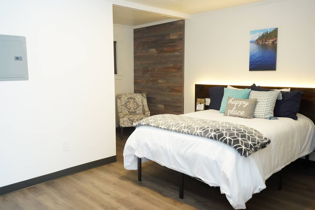 A bedroom with a bed, a headboard, a wall-mounted picture, and a chair.