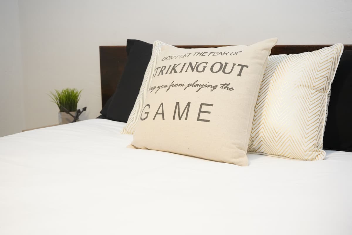 A bed with a pillow featuring motivational text, a small plant, and a dark headboard.