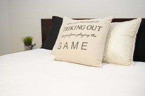 A bed with a pillow featuring motivational text, a small plant, and a dark headboard.