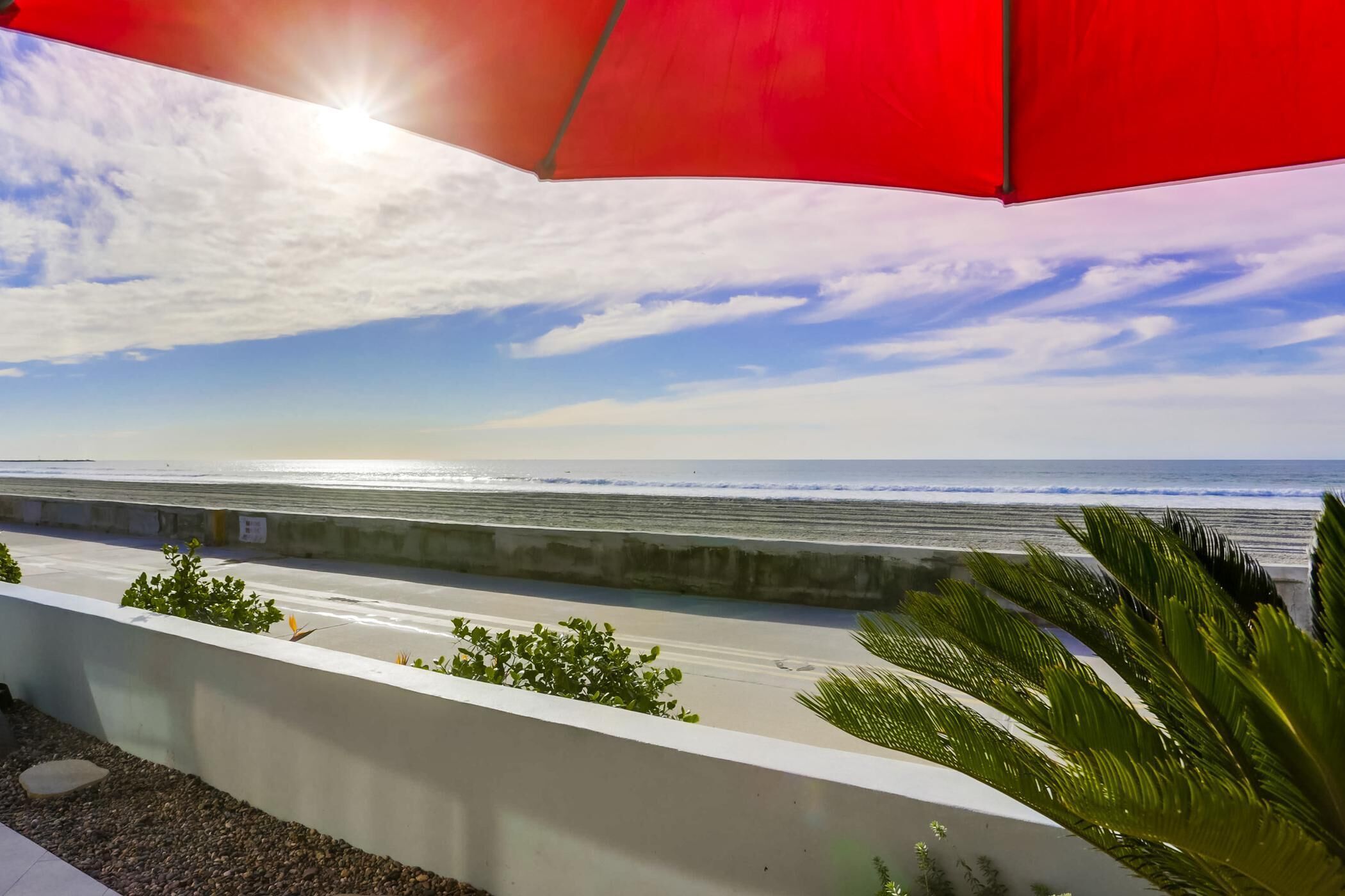 A coastal view with a concrete barrier, a red umbrella, and greenery.