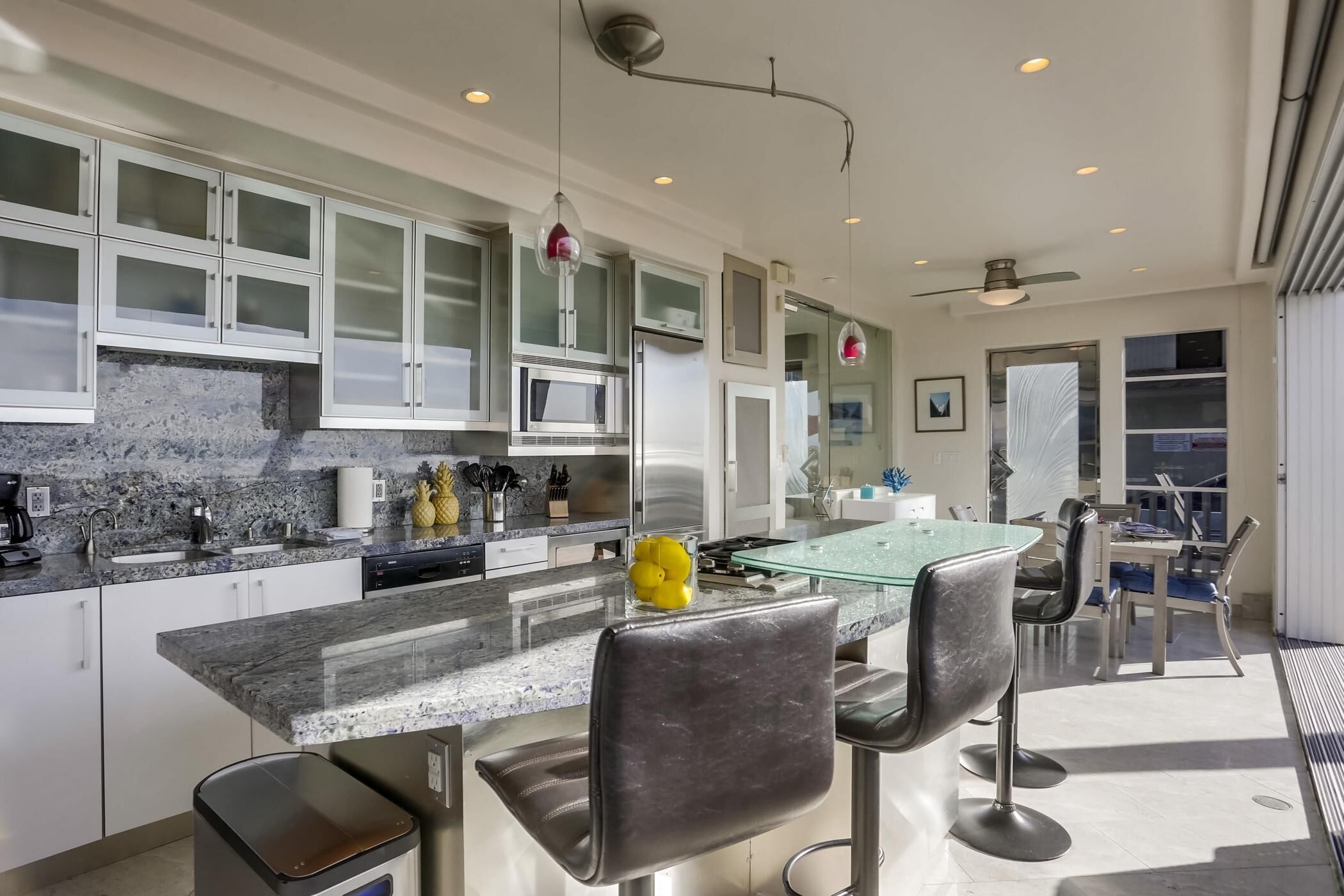 A modern kitchen with granite countertops, stainless steel appliances, and a glass dining table with bar stools.