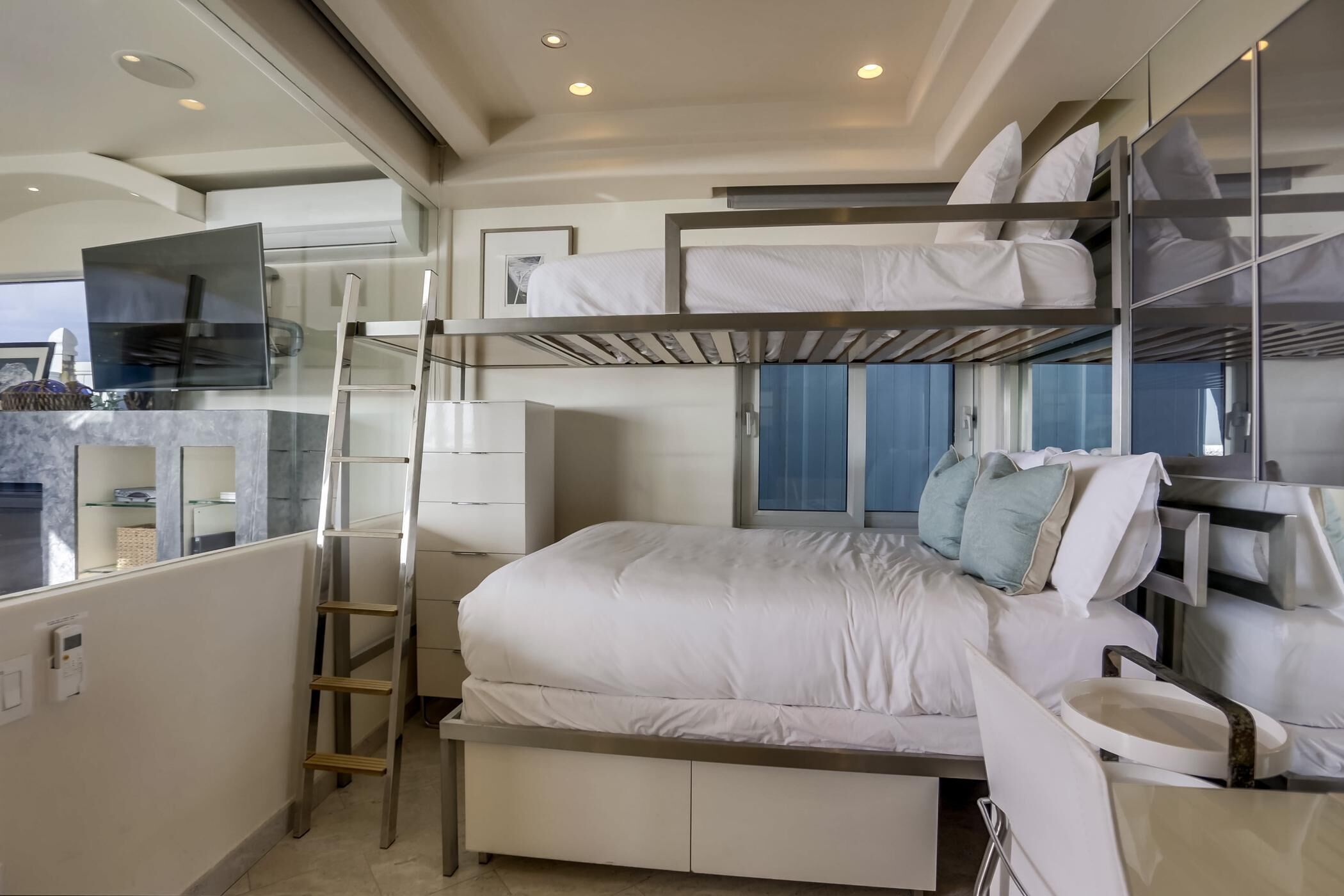 A compact hotel room with bunk beds, a desk, and a small kitchenette.
