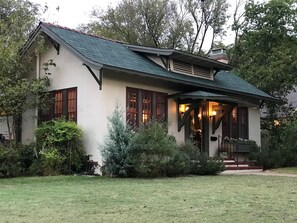 A two-story house with a steeply pitched roof, large windows, and a front porch with steps leading to the entrance. - Curated boutique stay in a 1920s English bungalow. Modern twist on a classic! (Waco)